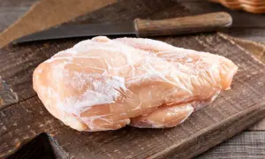 Zamrożona pierś kurczaka na drewnianej desce z nożem w tle.
