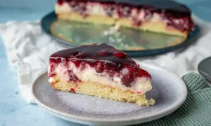 Ein saftiges Stück Kirsch Schmand Kuchen mit Kirschen und einer glänzenden Geleeschicht auf einem Teller.