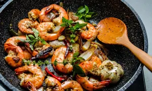 Gambas sautées à l'ail et au piment dans une poêle, prêtes pour le temps de cuisson. Une cuillère en bois est à côté.