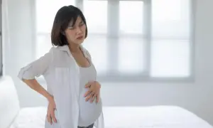 Kobieta w ciąży z rękami na plecach i brzuchu, cierpiąca z powodu skurczów porodowych.
