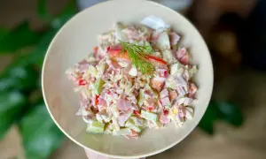 Pyszna sałatka z makaronem orzo, z szynką, jajkiem i warzywami, udekorowana gałązką koperku.