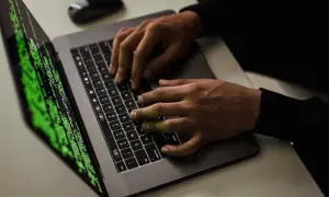 Ręce piszą kod na laptopie, ekran wyświetla zielony tekst. Czy to haker?