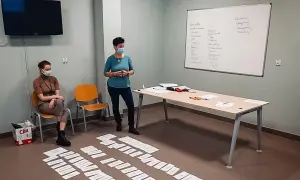 Trening zastępowania agresji: dwie kobiety w maseczkach, tablica z zapiskami, kartki na podłodze.