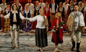 Grupa ludzi w strojach ludowych, mężczyzna w białej koszuli, kamizelce i spodniach z haftem, kobieta w kwiecistej sukni i halka.