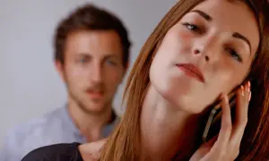 Kobieta rozmawia przez telefon, podczas gdy mężczyzna z tyłu patrzy z niepokojem. Jak żyć z narcyzem i mieć spokój?