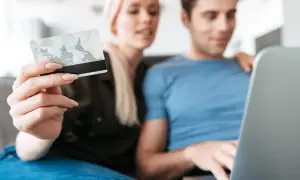 Kobieta trzyma kartę, mężczyzna pracuje na laptopie. Dane karty i PESEL to kluczowe informacje, jakie dane są potrzebne do wyłudzenia kredytu.