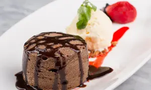 Un fondant au chocolat cœur coulant, servi avec une boule de glace à la vanille, une fraise et un coulis de fruits rouges.