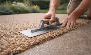 Mani che rifiniscono un pavimento esterno su ghiaia con una cazzuola, creando una superficie drenante e naturale.