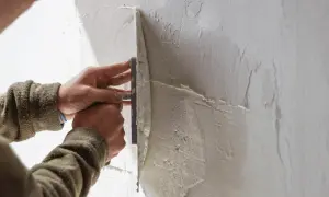 Mani esperte stendono il rasante su un muro, creando una superficie liscia e uniforme.