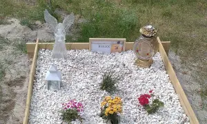 Nagrobek dla zwierzęcia z aniołem, zniczem, zdjęciem psa i kwiatami.