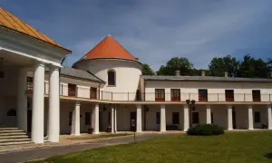 Zamek w Lesku z charakterystyczną okrągłą wieżą i arkadowym krużgankiem. Białe kolumny i pomarańczowy dach tworzą malowniczy widok.