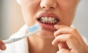 Een vrouw poetst haar tanden met een tandenborstel, zonder tandpasta. Ze trekt haar lip op om beter bij haar tanden te komen.