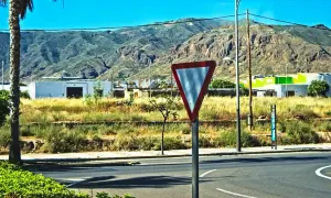 Señal de ceder el paso en una carretera con montañas al fondo.