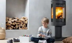 Chłopiec bawi się klockami przy nowoczesnym kominku, gdzie płonie ogień. Obok stos drewna, koszyk i kapcie. To przytulne miejsce, gdzie koza zamiast kominka tworzy ciepłą atmosferę.