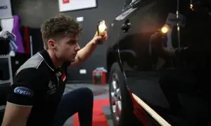 Detailer używa lampy, by ocenić stan lakieru. Widać drobne niedoskonałości na czarnym samochodzie.