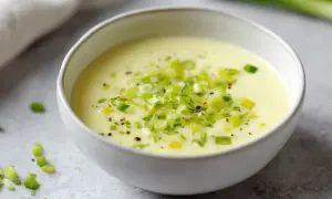Un bol de fondue de poireaux crémeuse, garnie de poireaux frais hachés et de poivre noir.