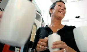 En kvinna ler glatt med en kaffemugg i handen. Hon verkar njuta av stunden, vilket visar vad betyder inflytande i vardagen.