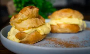 Zwei köstliche Windbeutel, gefüllt mit cremiger Vanillecreme, auf einem Teller mit Zimt bestäubt. Ein perfektes Windbeutel Rezept zum Nachmachen.