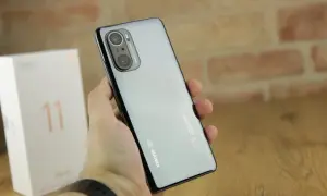 Dłoń trzyma błyszczący telefon Xiaomi 11i z potrójnym aparatem. Obok stoi białe pudełko z cyfrą 11.