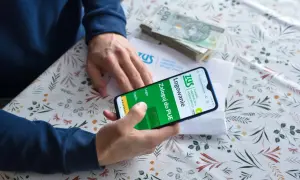 Słuchacz szkoły policealnej loguje się do PUE ZUS, by sprawdzić składki. Na stole stos banknotów.