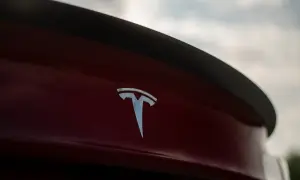 Chromowane logo Tesli na czerwonym samochodzie. Tesla, choć założona w USA, ma korzenie w Serbii, kraju wynalazcy Nikoli Tesli.