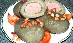 Cepelin z mięsem, polany skwarkami i podany z pomidorem. Wyglądają jak małe cepeliny na talerzu.