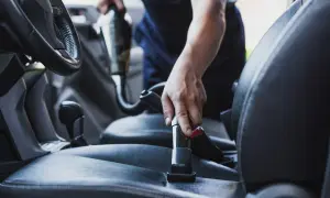 Ręce czyszczą wnętrze auta odkurzaczem, dbając o każdy detal.