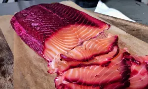 Rote Bete Lachs, mariniert und in Scheiben geschnitten, liegt auf Backpapier. Die leuchtend pinken Ränder des Lachses sind ein Blickfang.