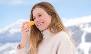 En hiver, faut-il mettre de la crème solaire ? Cette femme souriante en applique sur son visage, profitant d'un paysage enneigé.