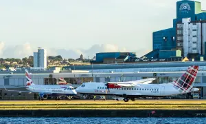 Zwei Flugzeuge, eines von British Airways, stehen auf dem Rollfeld. Im Hintergrund ist ein markantes blaues Gebäude mit der Aufschrift "Lyle's Golden Syrup" zu sehen. Welcher Flughafen London?