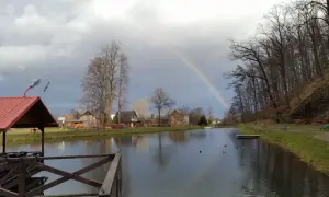Tęcza nad jeziorem u Bodzia Moszczanka. W oddali domki, po prawej las i ławki.