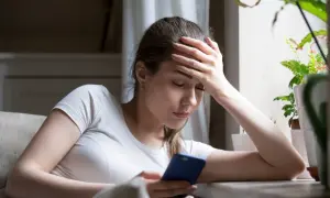 Zamyślona kobieta z ręką na czole, patrząca na telefon. Może to znak, po czym poznać, że ona chce odejść.
