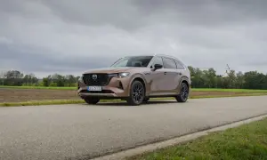 Brązowa Mazda CX80 na tle wiejskiego krajobrazu z kościołem w oddali.