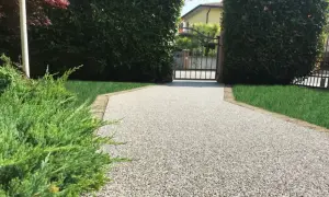Vialetto carrabile in pietra, con ghiaia chiara e bordi in cotto, conduce a un cancello in ferro battuto.