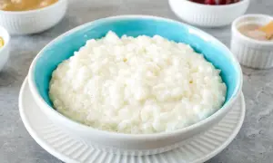 Cremiger Milchreis mit Risottoreis, serviert in einer blauen Schüssel, daneben Apfelmus und Preiselbeeren.