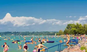 Tłum ludzi cieszy się słońcem i wodą na zatłoczonej balaton plaży. Wiele osób pływa, relaksuje się na materacach i bawi się w wodzie.