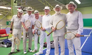 Sex äldre herrar i hattar och vita kläder poserar med tennisracketar, redo för en match i stil med Gustaf V:s tennis.