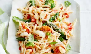 Trofie-Pasta mit Garnelen, Spargel und Tomaten, garniert mit Basilikum.