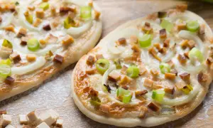 Zwei knusprige, vegetarische Flammkuchen mit Zwiebeln, Frühlingszwiebeln und würzigen Tofuwürfeln, bestreut mit etwas Mehl.
