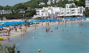 Lloret de Mar, lipiec: słoneczna pogoda zachęca do plażowania. Tłumy ludzi kąpią się i opalają na piaszczystej plaży, pod błękitnymi parasolami.