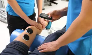 Fizjoterapeuta wykonuje zabieg fonoforezy na kolanie pacjenta, używając aparatu i elektrod.