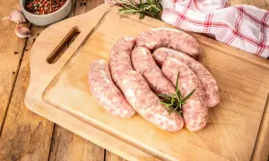 Surowe kiełbaski na desce, obok przyprawy i czosnku. Zastanawiasz się, jak długo parzyć kiełbasę, by była idealna?