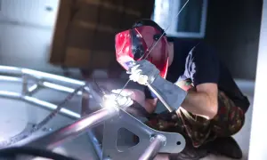 Spawacz w masce spawa aluminiową ramę. Widać jasny łuk spawalniczy i iskry. To pokazuje, czym spawać aluminium.