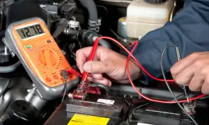 Mechaniker prüft mit Multimeter die Autobatterie, um den Anlasser wechseln zu können.
