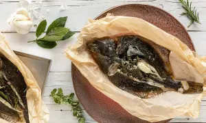 Two whole sole fish, seasoned and wrapped in parchment paper, with garlic and herbs.