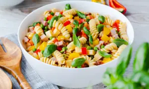 Bunter Nudelsalat ohne Mayo mit Spiralnudeln, Erbsen, Paprika und Schinkenwürfeln, garniert mit Basilikum.