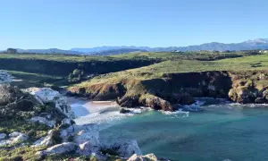 Acantilados y mar turquesa, ideales para rutas senderismo San Vicente de la Barquera. Paisaje costero con verdes colinas y montañas al fondo.