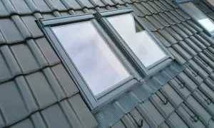 Dwa okna dachowe balkonowe w ciemnej dachówce, odbijające niebo.