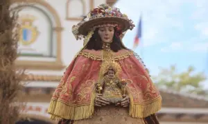 Virgen del Rocío pastora, con su manto rosa bordado y el Niño Jesús en brazos, adornada con flores y un sombrero.