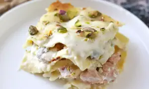 Porzione di lasagne bianche sfiziose con pistacchi e un ripieno cremoso, servite su un piatto bianco.